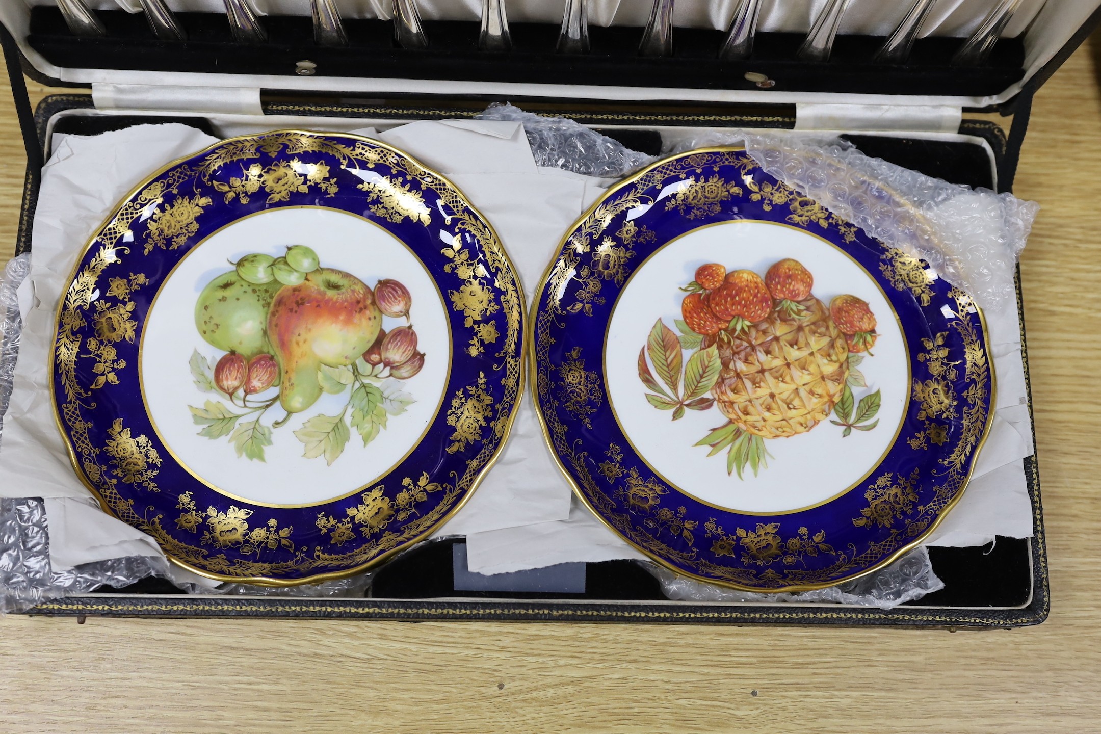 A cased dessert service containing six gilt and fruit decorated plates and a set of knives and forks